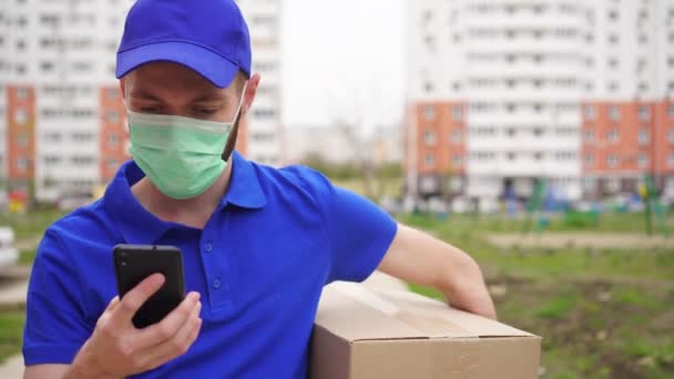 doručovatel v ochranné lékařské masce na tváři používá smartphone - Záběry, video