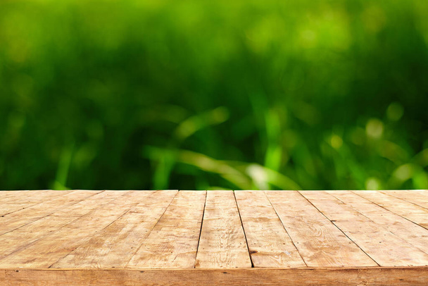 Порожній дерев'яний стіл палуби з фоном боке листя. Готовий до відображення продукту монітор
. - Фото, зображення