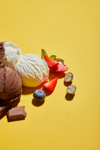 leckeres braunes und weißes Eis mit Beeren, Schokolade und Minze auf gelbem Hintergrund - Foto, Bild