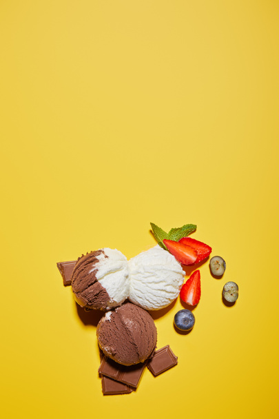top view of tasty brown and white ice cream with berries, chocolate and mint on yellow background - Foto, afbeelding