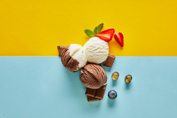 felülnézet ízletes barna és fehér fagylalt bogyókkal, csokoládé és menta sárga és kék háttér - Fotó, kép