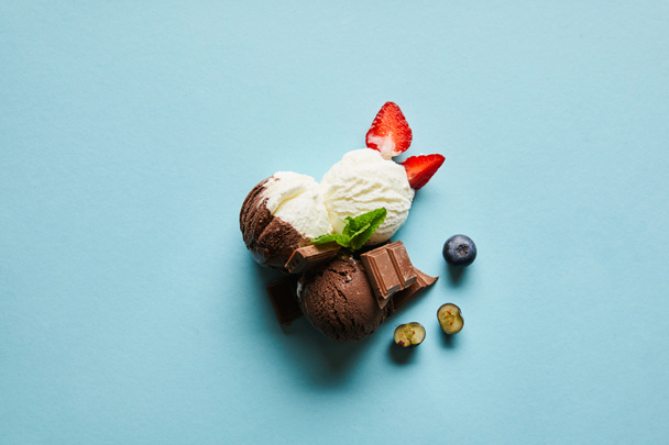 top view of tasty brown and white ice cream with berries, chocolate and mint on blue background - Foto, Imagem