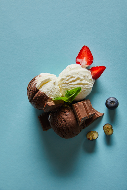 top view of tasty brown and white ice cream with berries, chocolate and mint on blue background - Fotografie, Obrázek