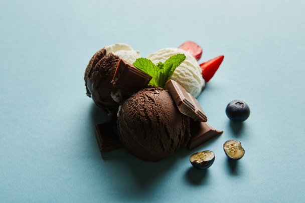 ízletes barna és fehér fagylalt bogyókkal, csokoládé és menta kék alapon - Fotó, kép