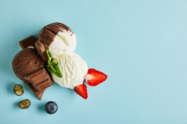 top view of tasty brown and white ice cream with berries, chocolate and mint on blue background - Foto, Imagen