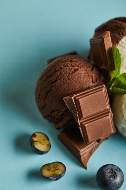 close up view of tasty brown ice cream with berries, chocolate and mint on blue background - Foto, imagen