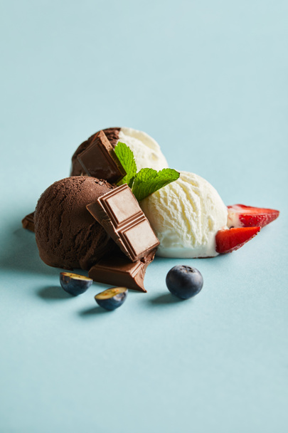 tasty brown and white ice cream with berries, chocolate and mint on blue background - Fotó, kép