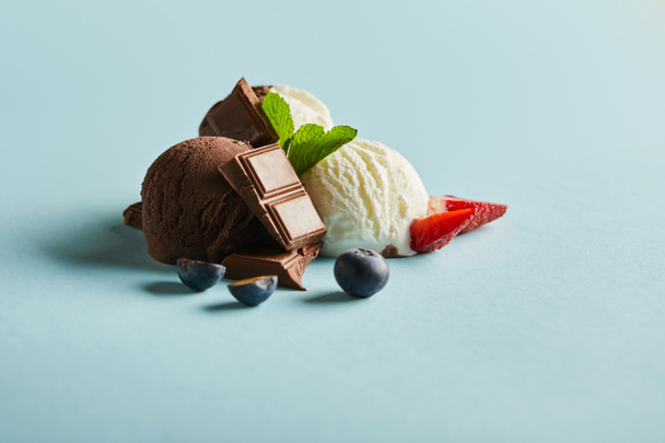saboroso sorvete marrom e branco com bagas, chocolate e hortelã no fundo azul
 - Foto, Imagem