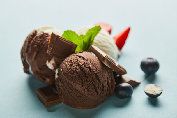szelektív fókusz ízletes barna és fehér fagylalt bogyókkal, csokoládé és menta a kék háttér - Fotó, kép