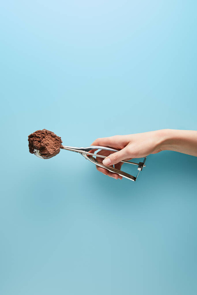 καλλιεργημένη άποψη της γυναίκας κρατώντας σέσουλα με παγωτό σοκολάτα σε μπλε φόντο - Φωτογραφία, εικόνα