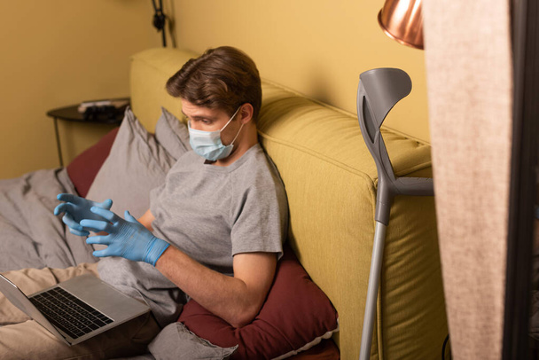 Selectieve focus van gehandicapte man in medisch masker met videogesprek op laptop op bed  - Foto, afbeelding