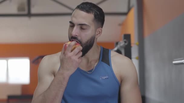 Close-up of handsome Middle Eastern sportsman with brown eyes biting red apple and chewing. Portrait of confident happy man eating fruit after training. Sport, lifestyle, health. - Imágenes, Vídeo