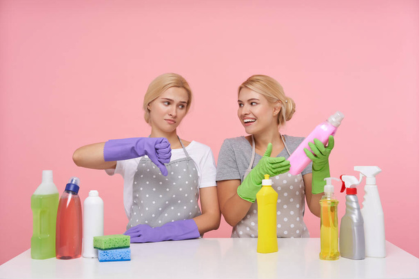 Indoor shot młodych białogłowych kobiet z przypadkowej fryzury ubrany w mundur podczas pozowania na różowym tle, przygotowanie do wiosennego czyszczenia i wybór detergentów - Zdjęcie, obraz