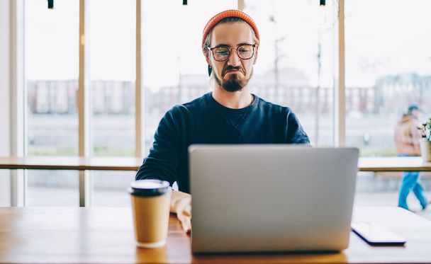 Male freelancer feeling envy while checking rating of successful workers of month on website of company connected to public wifi internet on laptop device, hipster guy watching online video - Foto, Bild