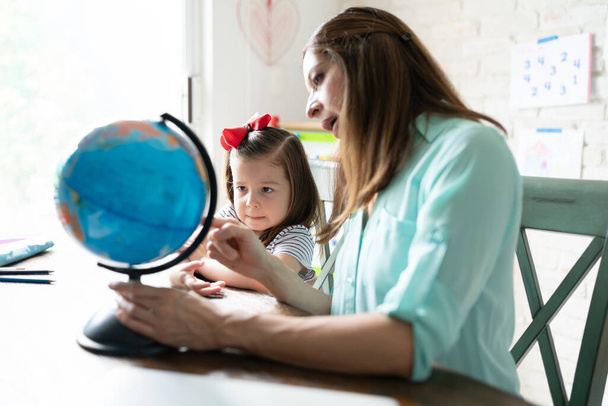 mooi weinig drie jaar oud wordt thuis onderwezen door haar moeder en leren over de wereld met behulp van een globe - Foto, afbeelding