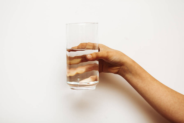 A woman's hand holds a glass of water on a dark background - Photo, Image