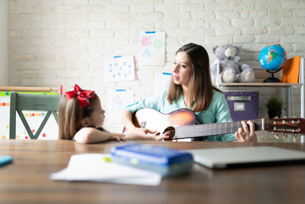 Muotokuva kaunis äiti soittaa kitaraa ja opettaa musiikkia hänen pieni tyttö kotona
 - Valokuva, kuva