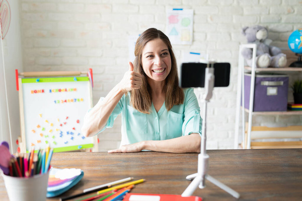 Caucasian female teacher giving thumbs up and saying good job to her students while on a video call on her smartphone - Photo, Image