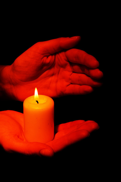 Burning candle in hands isolated on black - Фото, изображение