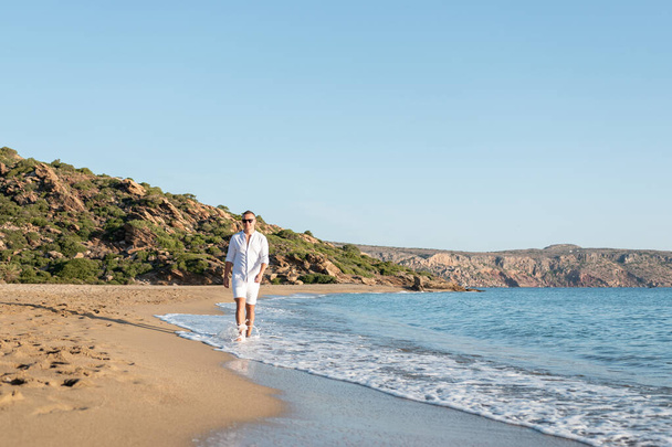 Handsome happy man in white shirt walking on the beach. Summer vacations concept. - 写真・画像