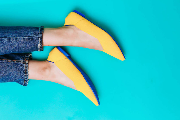 beautiful female legs are dressed in stylish yellow shoes without a heel. Light yellow summer sandals on a blue background. - Fotografie, Obrázek