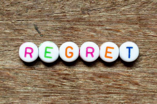 Weiße Perle mit farbigem Buchstaben in Wort Bedauern auf Holzgrund - Foto, Bild