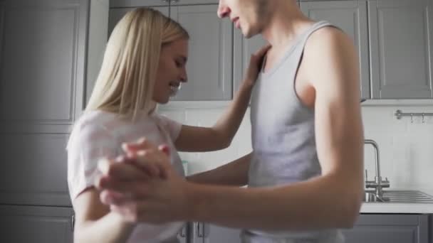 Attractive young joyful couple have romantic dancing while cooking in the kitchen at home - Felvétel, videó