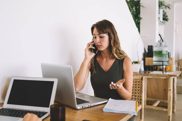 Serious female remote worker reading message with information about software updating calling to personal programmer for discussing details and solving online problems, concept of business talking - Foto, Imagem