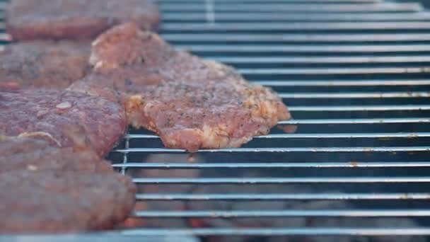 Grillsütő. Egy férfi hússzeletet és húsgombócot süt hamburgernek, megfordítja a húst fogóval.. - Felvétel, videó