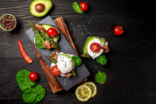 Italiaans eten: snack toastjes met avocado, asperges en gebakken ei, bovenaanzicht. Achtergrond van het voedselrecept. - Foto, afbeelding