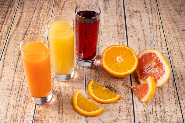 Orange, pineapple and cherry juices in glass glasses. Orange and grapefruit are citrus fruits and many vitamins. - Photo, Image