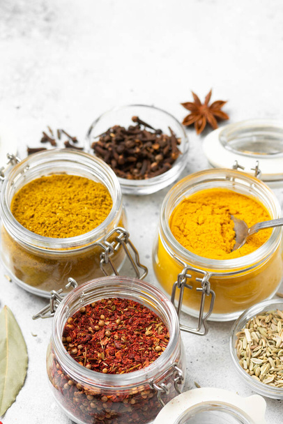 Spices and condiments in glass jars on a light gray table. Spices: turmeric, curry, star anise, fennel and cloves close-up with space for text - Foto, Imagen
