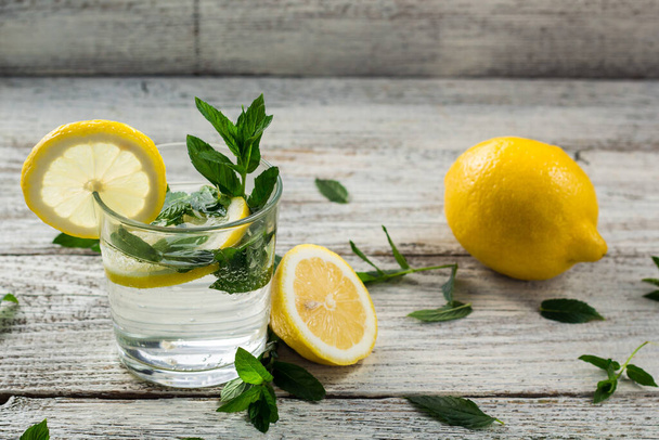 Wasser mit Zitrone und Minze in einem Glas auf Holzgrund. Sommerfrisches Limonadengetränk mit Stroh. Kopierraum - Foto, Bild