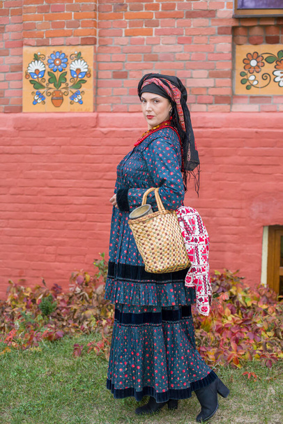 Woman with a basket in retro clothes of the 19th century. Antique clothing of the late 19th century. Beautiful dress and skirt on a woman. Beads and decoration on a girl. Ancient place. Tradition and - Photo, Image