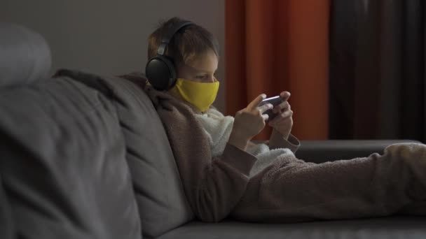 Der Mann mit der Schutzmaske sitzt auf der Couch und hört über Kopfhörer Musik. Quarantäne 2020 - Filmmaterial, Video