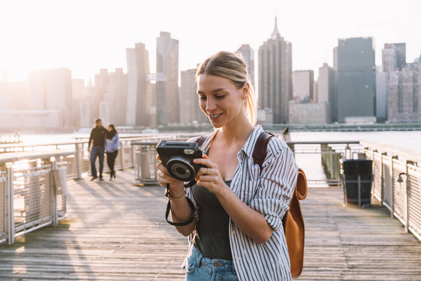 Happy woman tourist with old fashioned instant camera feeling good during time for exploring urban setting in America, successful young photographer editing pictures made with retro technology - Foto, immagini