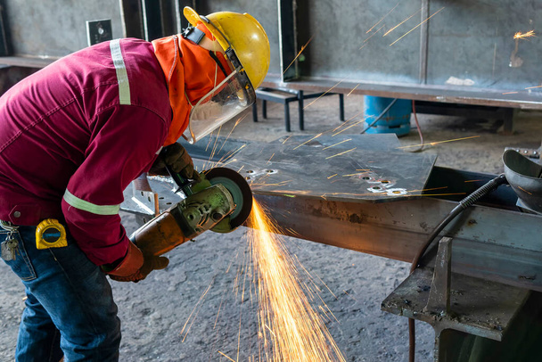 İşçi, endüstriyel fabrikada kestikten sonra çelik levhanın yüzeyini öğütmek için öğütme makinası kullanılıyor.. - Fotoğraf, Görsel