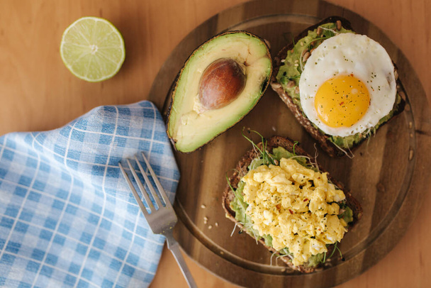 Different cooked egg on avocado sandwich with whole grain bread on wooden board. Top view - 写真・画像