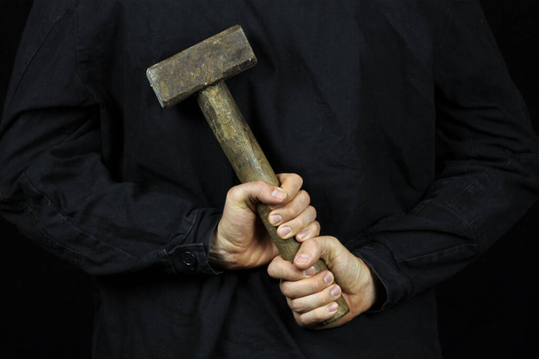 Een man houdt een moker vast, een hamer achter zijn rug om op een zwarte achtergrond - Foto, afbeelding