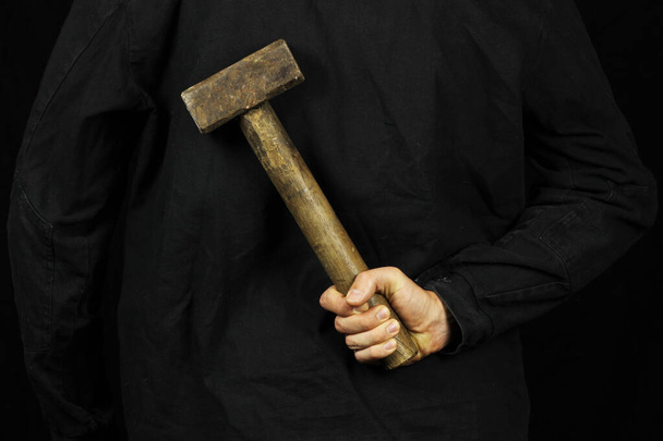 Un hombre sostiene un martillo, un martillo detrás de su espalda sobre un fondo negro
 - Foto, imagen