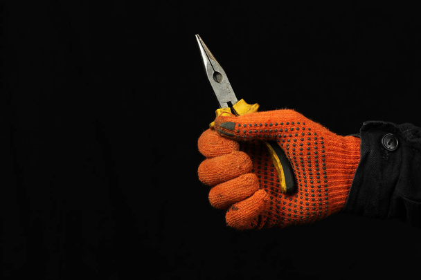 Ένα χέρι γάντια κρατά ένα ζευγάρι πένσες σε μαύρο φόντο από κοντά - Φωτογραφία, εικόνα
