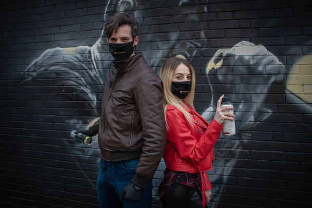 masked guy and girl on the background of graffiti with spray cans of paint. - Photo, Image