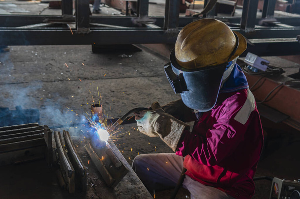 Зварювач зварює сталеву конструкцію з процесом Flux Cored Arc Welding (FCAW) і одягається належним чином з особистим захисним обладнанням (PPE) для безпеки, на промисловому заводі. - Фото, зображення