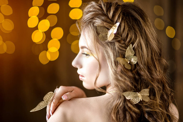 Portrait of young sexy girl with golden butterflies on curly hair at yellow background. Fashion and fairy photoshoot. - Фото, зображення