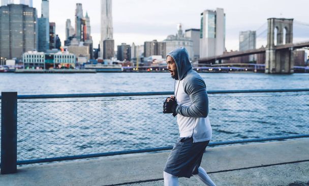 Side view of serious athletic ethnic fighter in modern comfy sport clothes  training in city on river embankment at dawn - Foto, Imagem