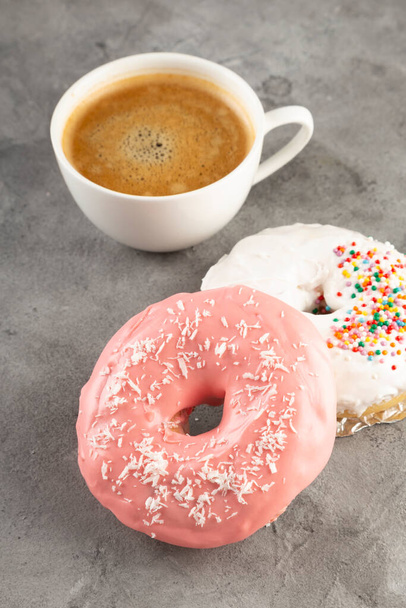 White cup of coffee and two donuts in white and pink icing on grey background - Photo, image