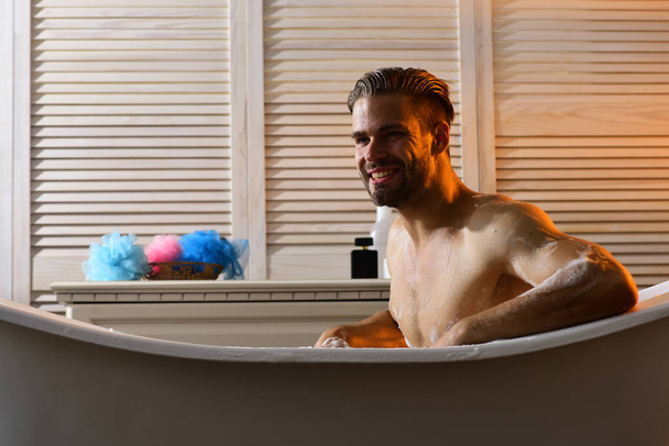 Macho sitting naked in bathtub and smiling - Foto, afbeelding
