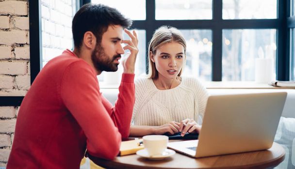 Serious male and female entrepreneurs cooperating indoors discussing details for common project while reading information on website, skilled freelancers working remotely brainstorming on program code - Фото, изображение