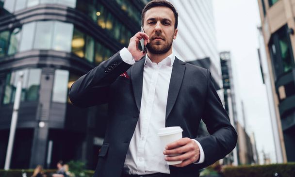 Half length portrait of serious proud ceo looking at camera while solving enterprise problems during international business conversation, lawyer with coffee to go phoning to operator for consultancy - Foto, Imagen
