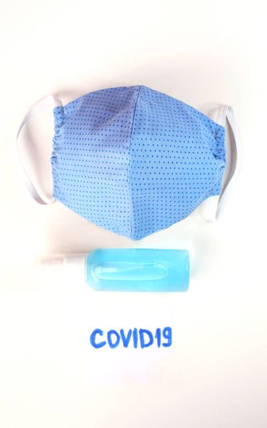 Cloth cotton face mask and antibacterial gel sanitizer to prevent coronavirus Covid 19. Hand made face mask blue color on white background. - Valokuva, kuva